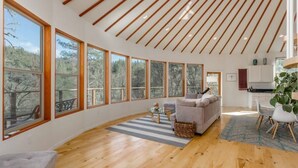 Un amplio salón con ventanas grandes, techo de madera y una zona de estar acogedora.