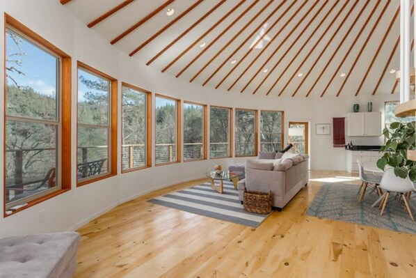 A spacious living room with large windows, a wooden ceiling, and a cozy seating area. - Stunning Roundhouse, Waterfall, Hot Tub & Views (Grass Valley)