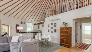 Amplia sala de estar con sofá gris, piso de madera y techo alto con vigas de madera.