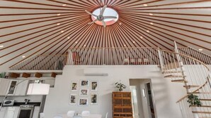 Un interior moderno con un diseño de techo radial, un ventilador de techo central, una escalera y una zona de cocina.