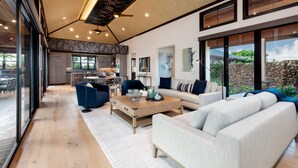 A modern living room with a large sofa, a coffee table, and a dining area with chairs. - Luxury Nohea Home w/ Pool & private 2 BR Ohana
Access to Mauna Lani Sports Club! (Kamuela)