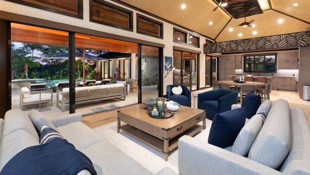 A modern living room with a large sofa, a coffee table, and a dining area with a kitchen in the background. - Luxury Nohea Home w/ Pool & private 2 BR Ohana
Access to Mauna Lani Sports Club! (Kamuela)