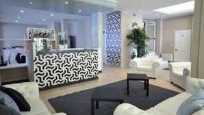 En moderne hotellobby med receptionsdisk, hvide sofaer, et sofabord og en væg med et mønster.