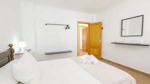 Una habitación de hotel ordenada con una cama, una mesita de noche, una lámpara, un perchero para toallas, una puerta y un espejo en la pared.