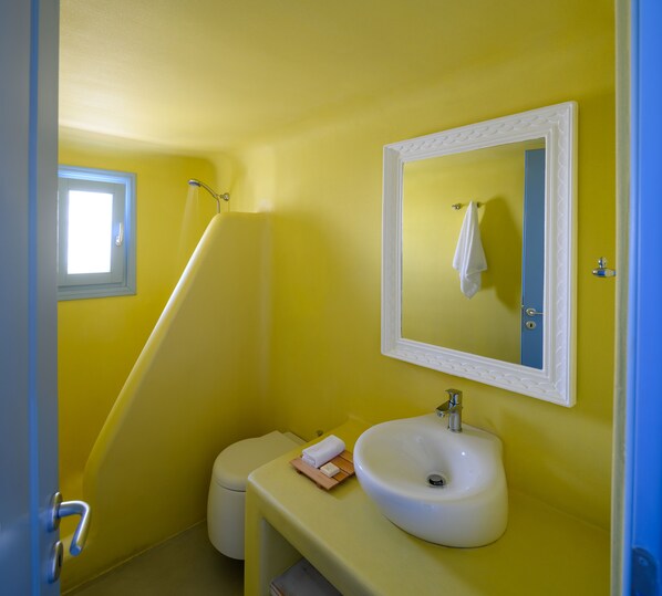 Un baño con una pared amarilla, un lavamanos blanco, un espejo y una ventana.