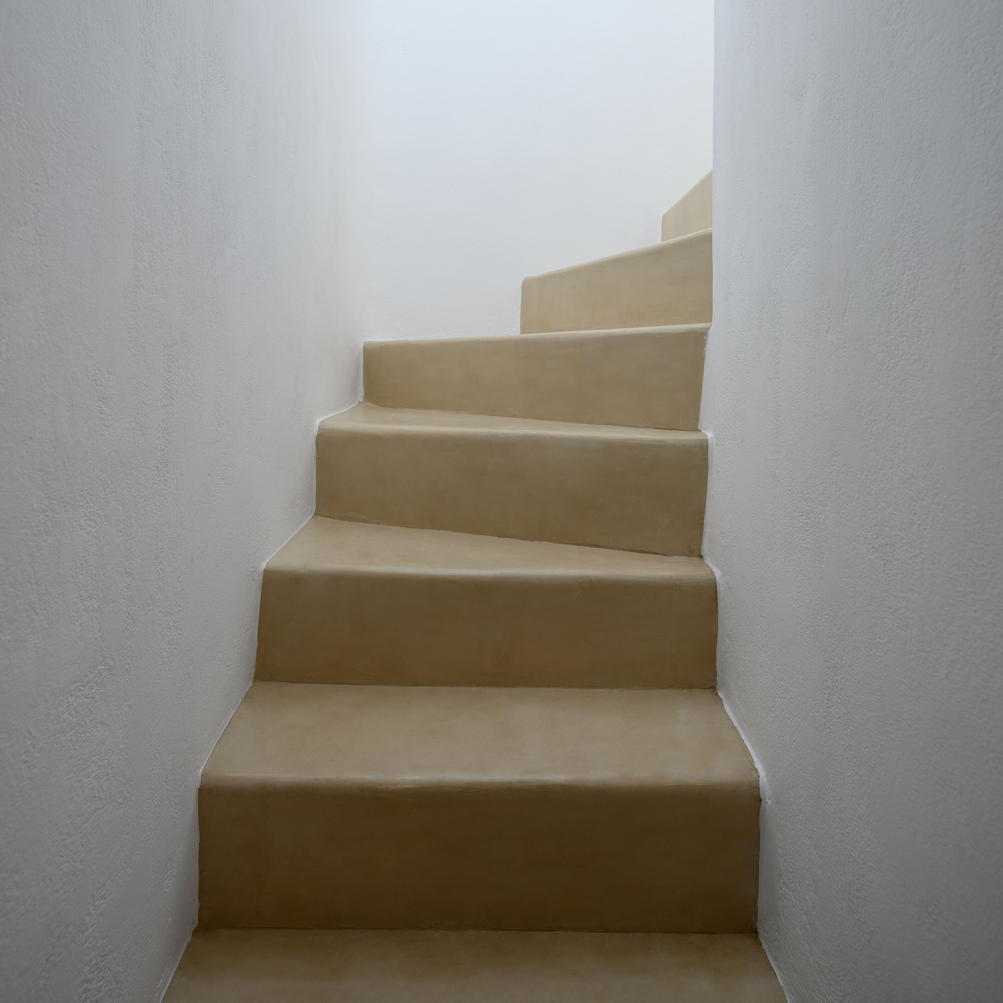 Un conjunto de escaleras beiges que conducen hacia arriba en un estrecho pasillo de paredes blancas.