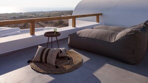 A balcony with a view of the landscape, a wooden railing, a round table with a glass, and a sofa with cushions. - Este Luxury Suites (Santorini)