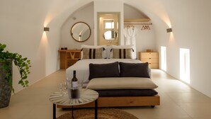 A modern bedroom with a large bed, bedside tables, a mirror, and a small table with a bottle and glasses. - Este Luxury Suites (Santorini)