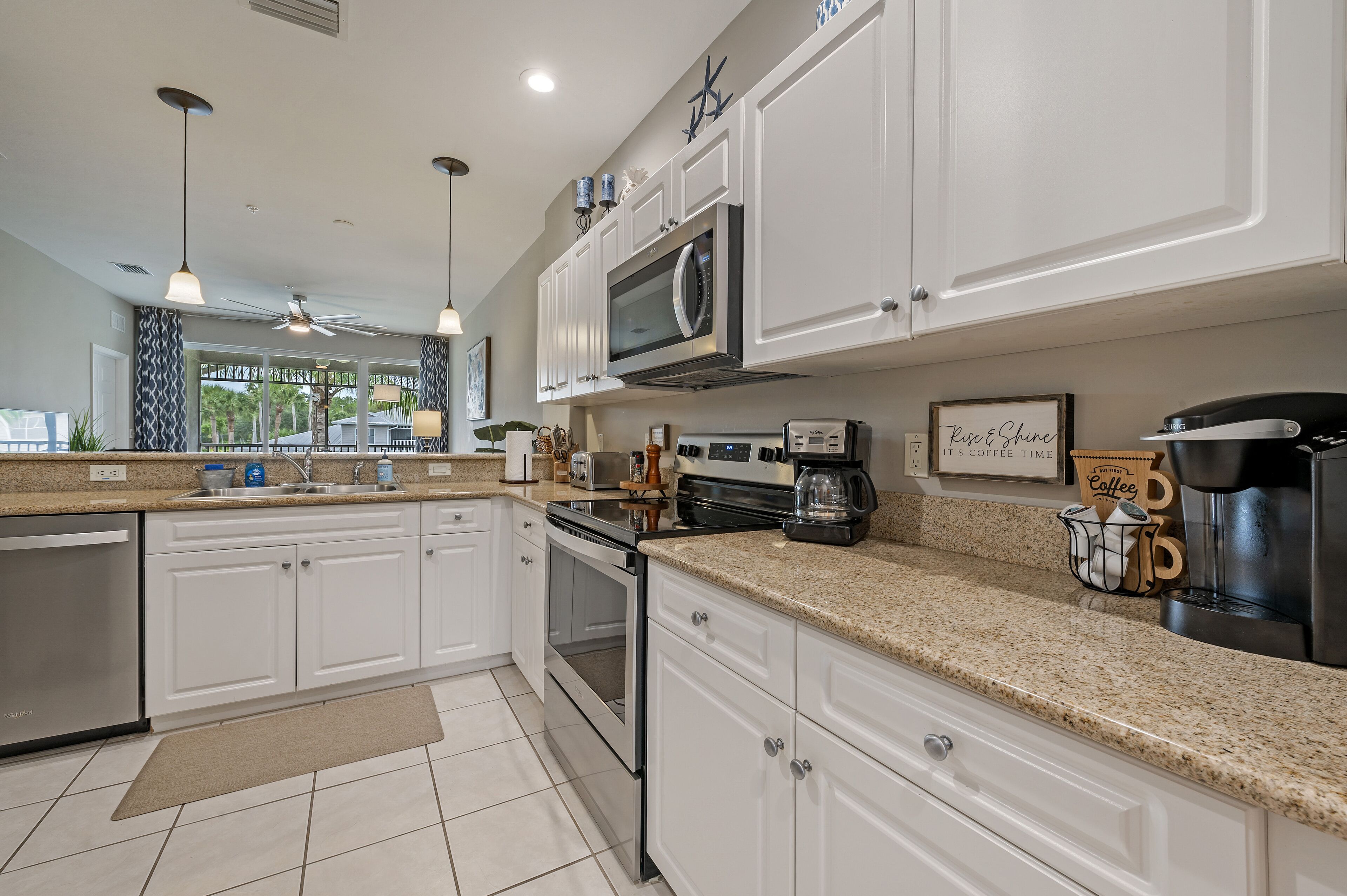 A modern kitchen with white cabinets, granite countertops, stainless steel appliances, and pendant lighting.