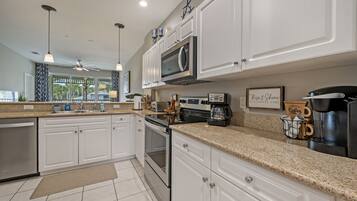A modern kitchen with white cabinets, granite countertops, stainless steel appliances, and pendant lighting.