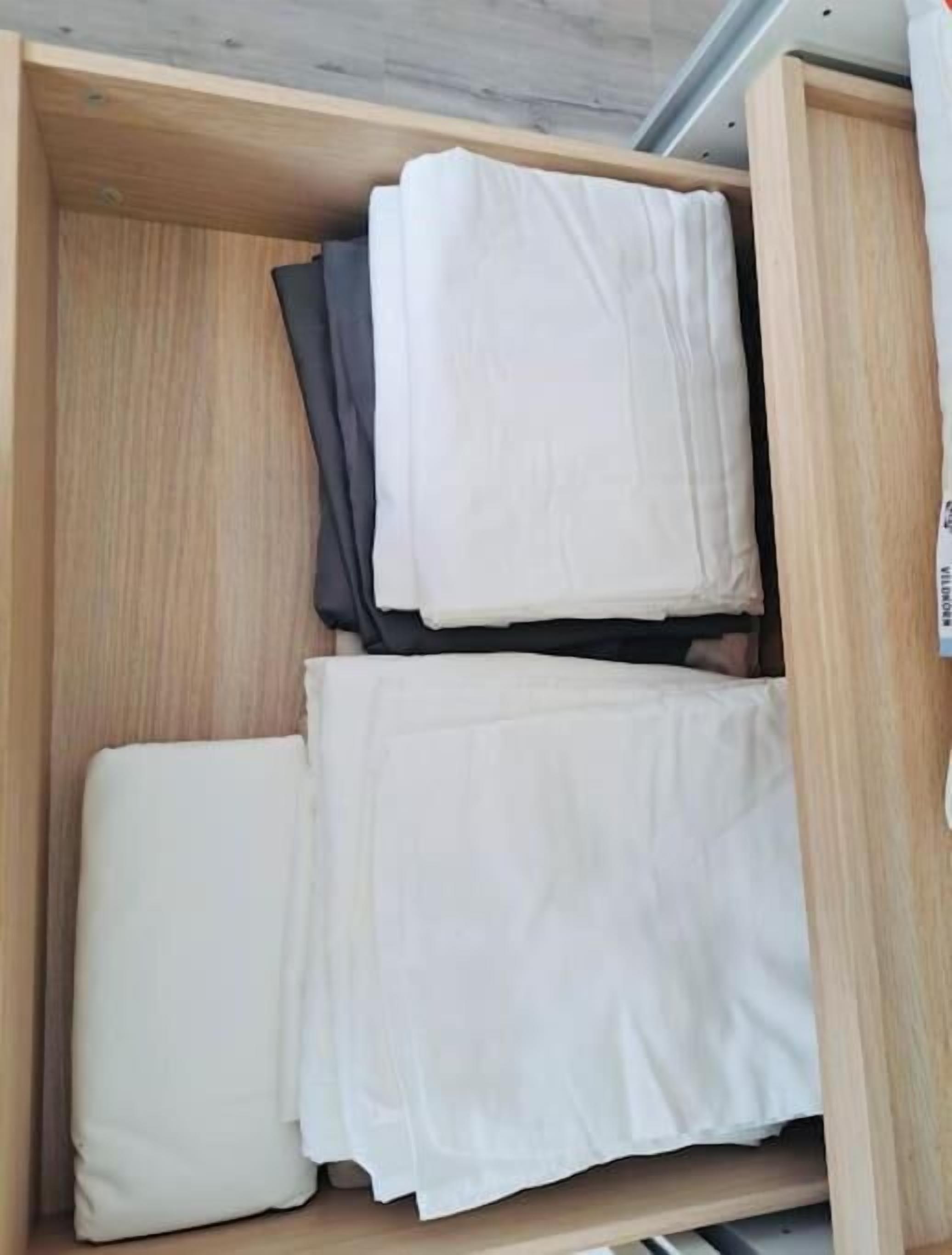 A wooden storage unit with folded white and dark-colored linens.