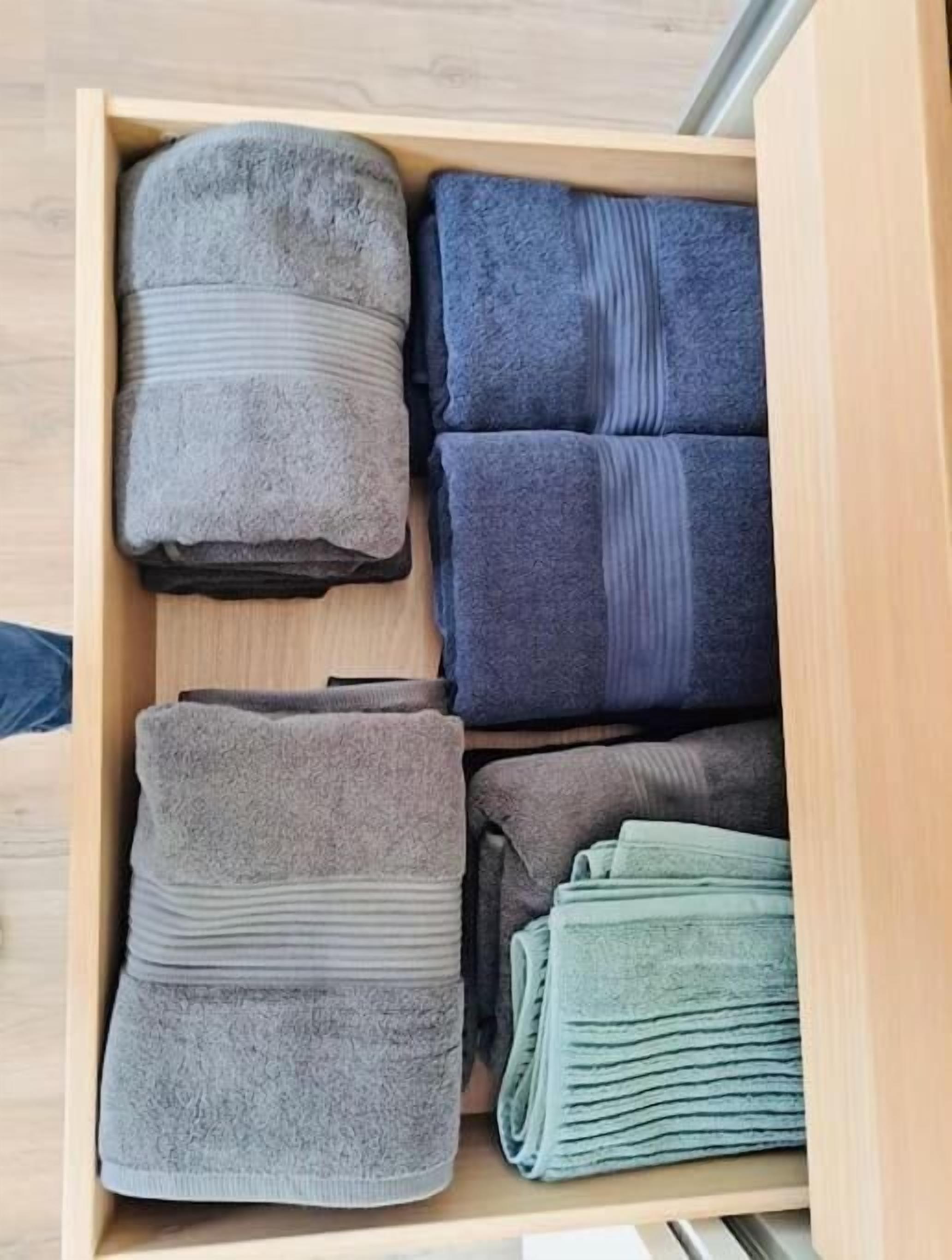 A drawer with neatly folded towels in various shades of gray and blue.