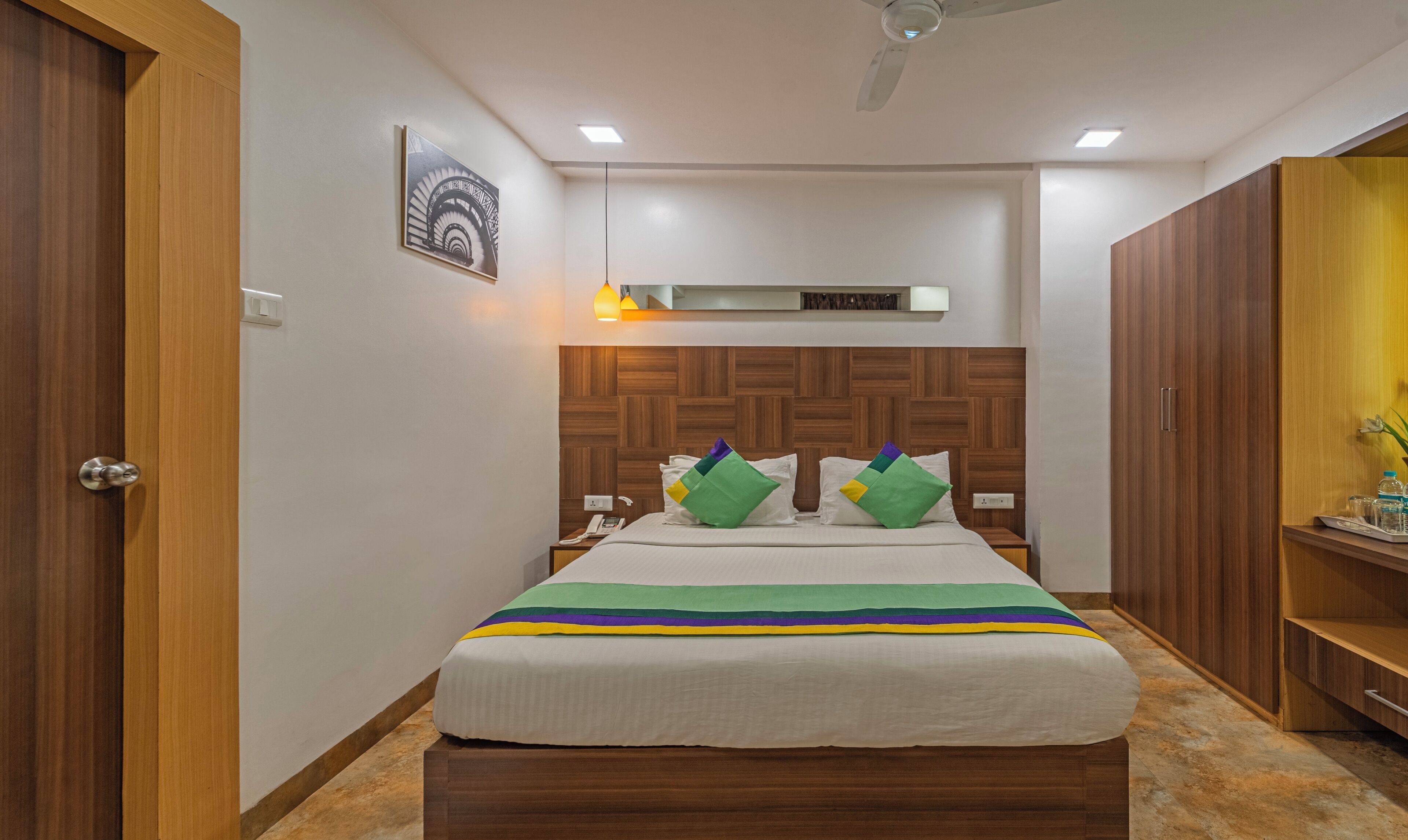 Una habitación de hotel ordenada con cama, cabecero de madera y una mesita de noche pequeña.
