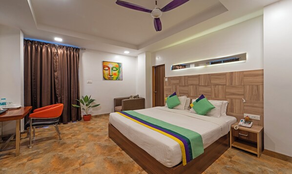 Habitación de hotel con cama, escritorio, silla, ventilador de techo y un cuadro en la pared.