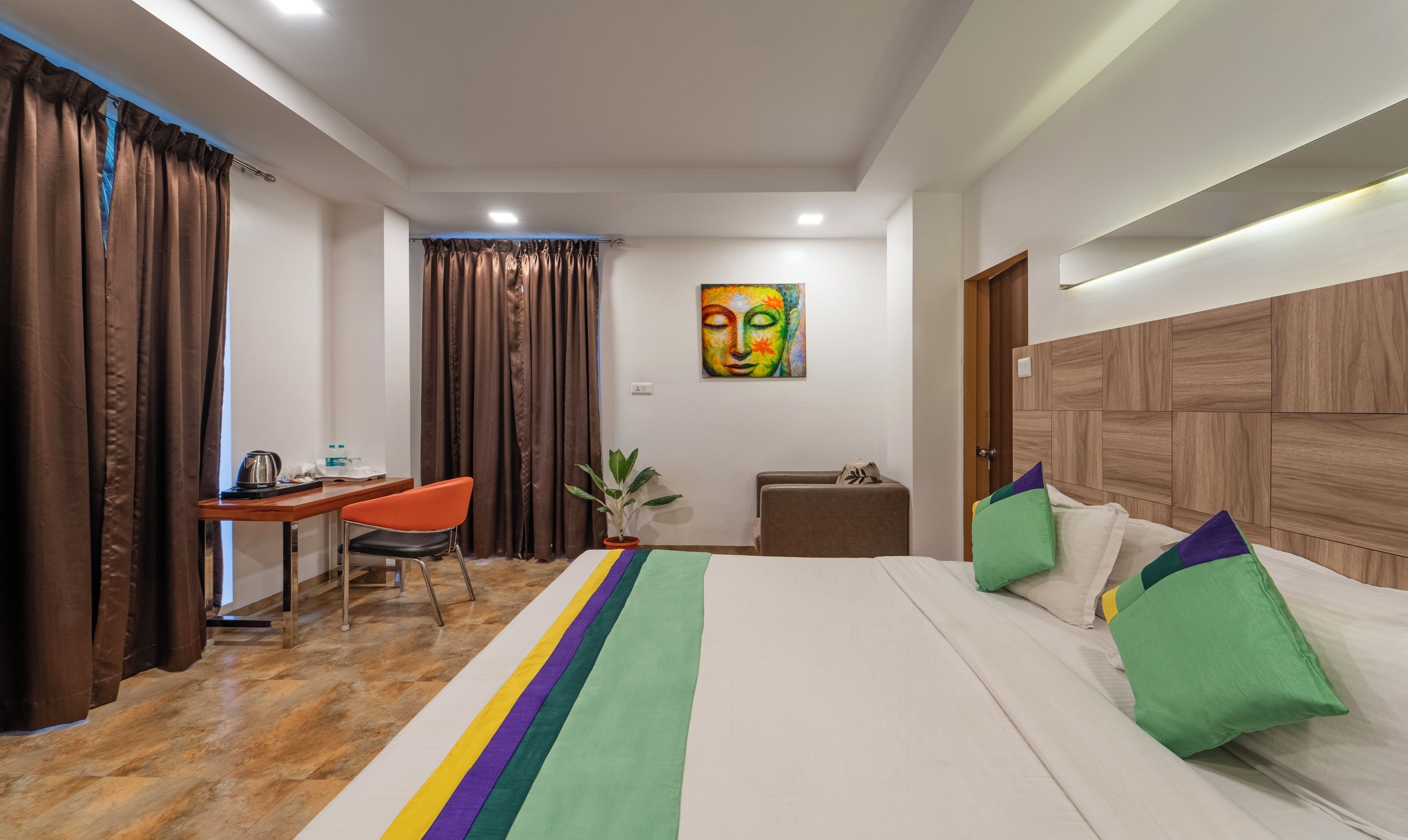 Hotelkamer met een bed, bureau, stoel, een potplant en een schilderij aan de muur.