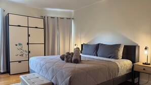 Une chambre à coucher avec un lit, une table de chevet avec une lampe, une armoire et une fenêtre avec des rideaux.