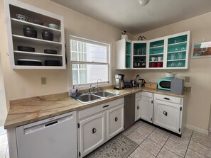 Una cocina con armarios blancos, lavavajillas integrado, una ventana y un microondas.
