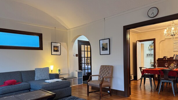 Un salon comprenant un canapé, un fauteuil et une table basse, un coin repas avec une table et des chaises, et un couloir menant à une autre pièce.