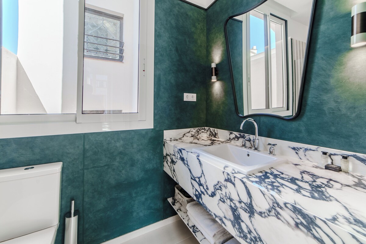A bathroom with a white marble sink, a mirror, and teal walls.