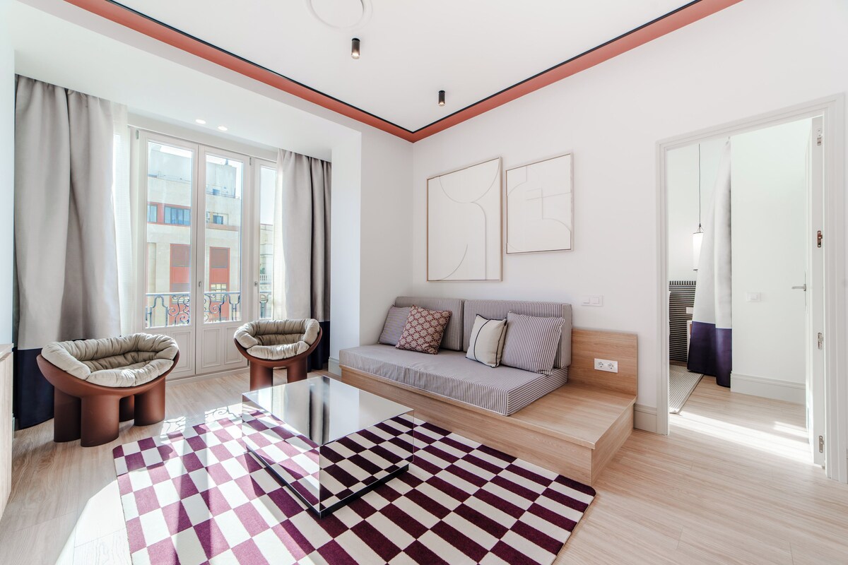 Una sala de estar moderna con un sofá, dos sillones, una mesa de centro de vidrio y una alfombra estampada.