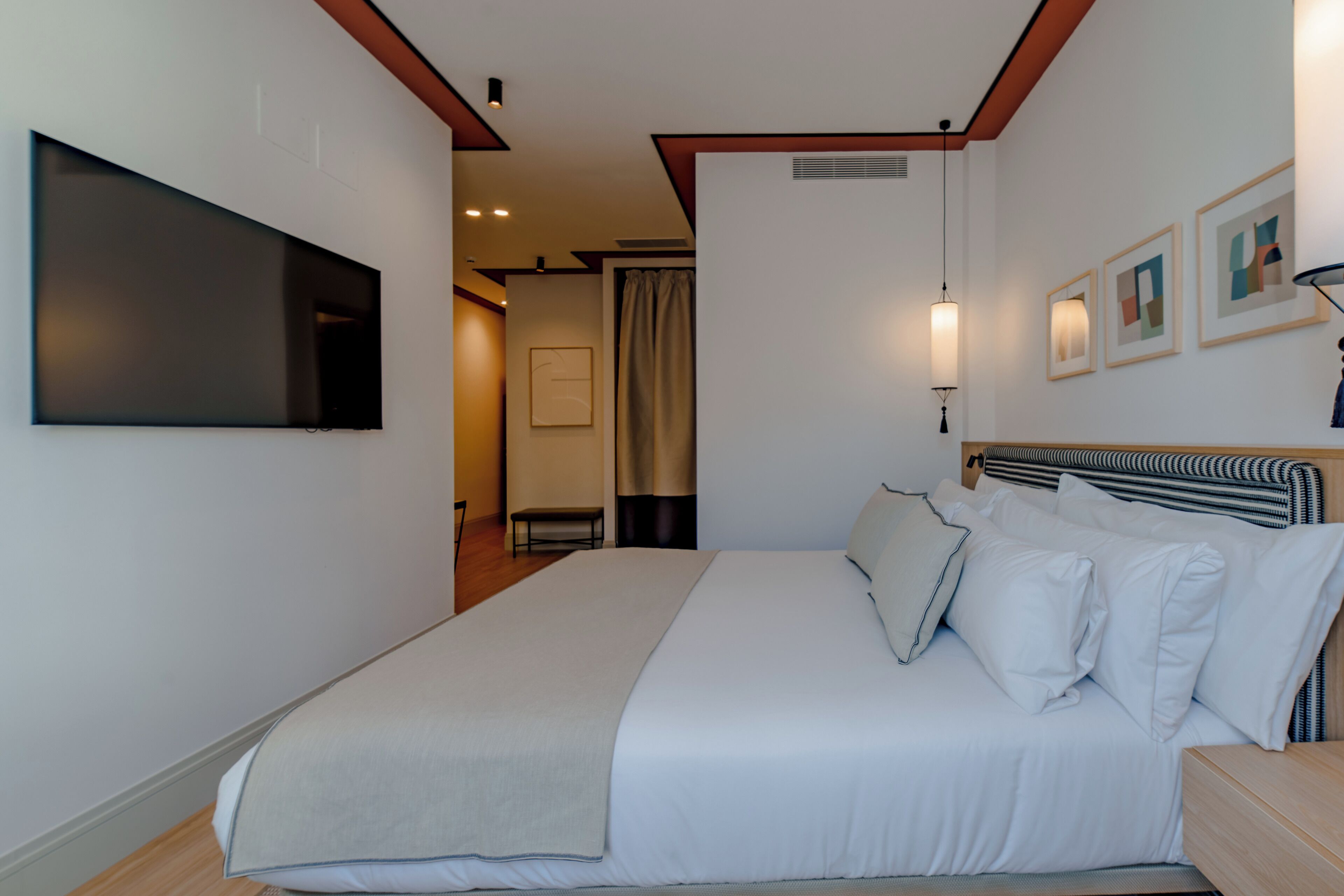 Ein modernes Hotelzimmer mit einem großen Bett, einem flachbildfernseher an der Wand und einer kleinen Sitzecke mit Sessel und Tisch.