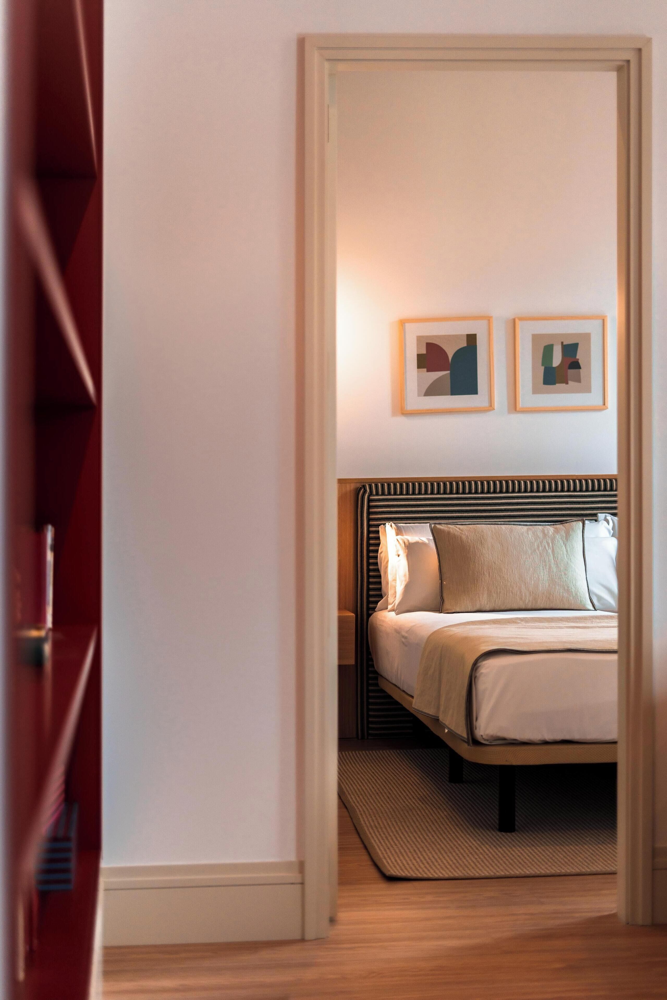 A hotel room with a bed, a nightstand, and two framed artworks on the wall.
