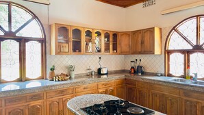 A kitchen with wooden cabinets, a granite countertop, a gas stove, and a window with a decorative grill. - Starehe Villa (Arusha)