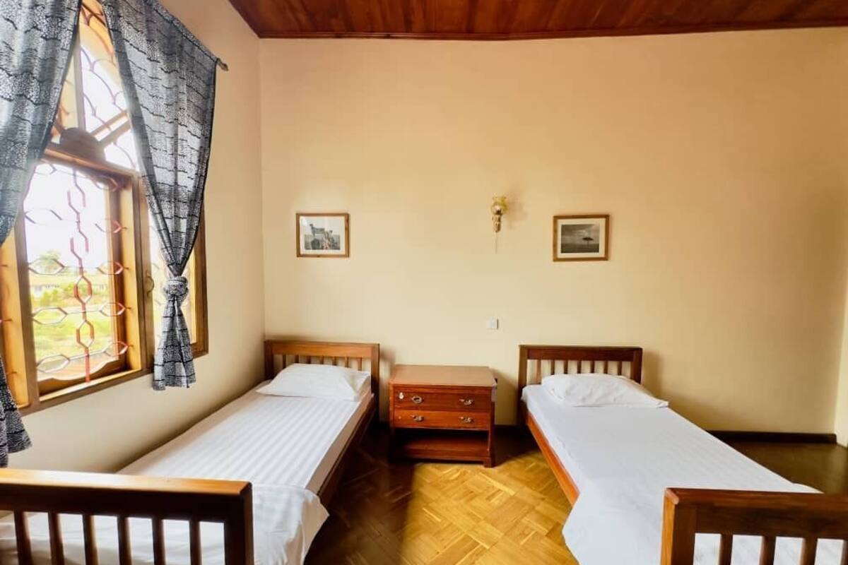 A room with two single beds, a wooden dresser, and a window with curtains.