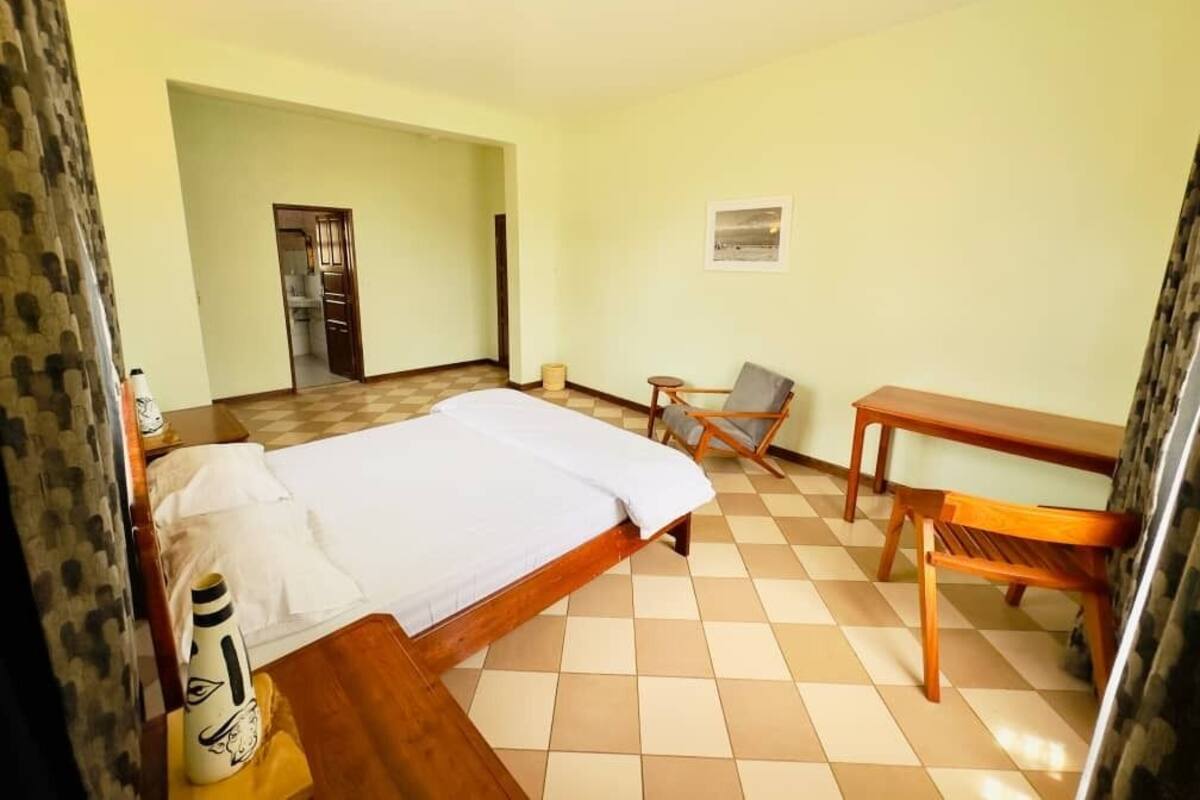 A hotel room with a bed, a chair, a table, and a small table lamp.