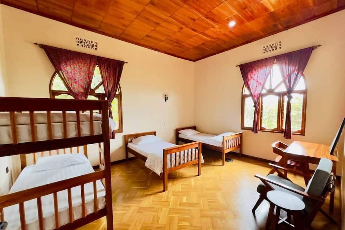 A room with three wooden bunk beds, a desk with a chair, and two windows with curtains.