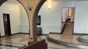 Un hall d’entrée spacieux avec un plafond haut, un escalier central et un espace détente avec un banc marron.