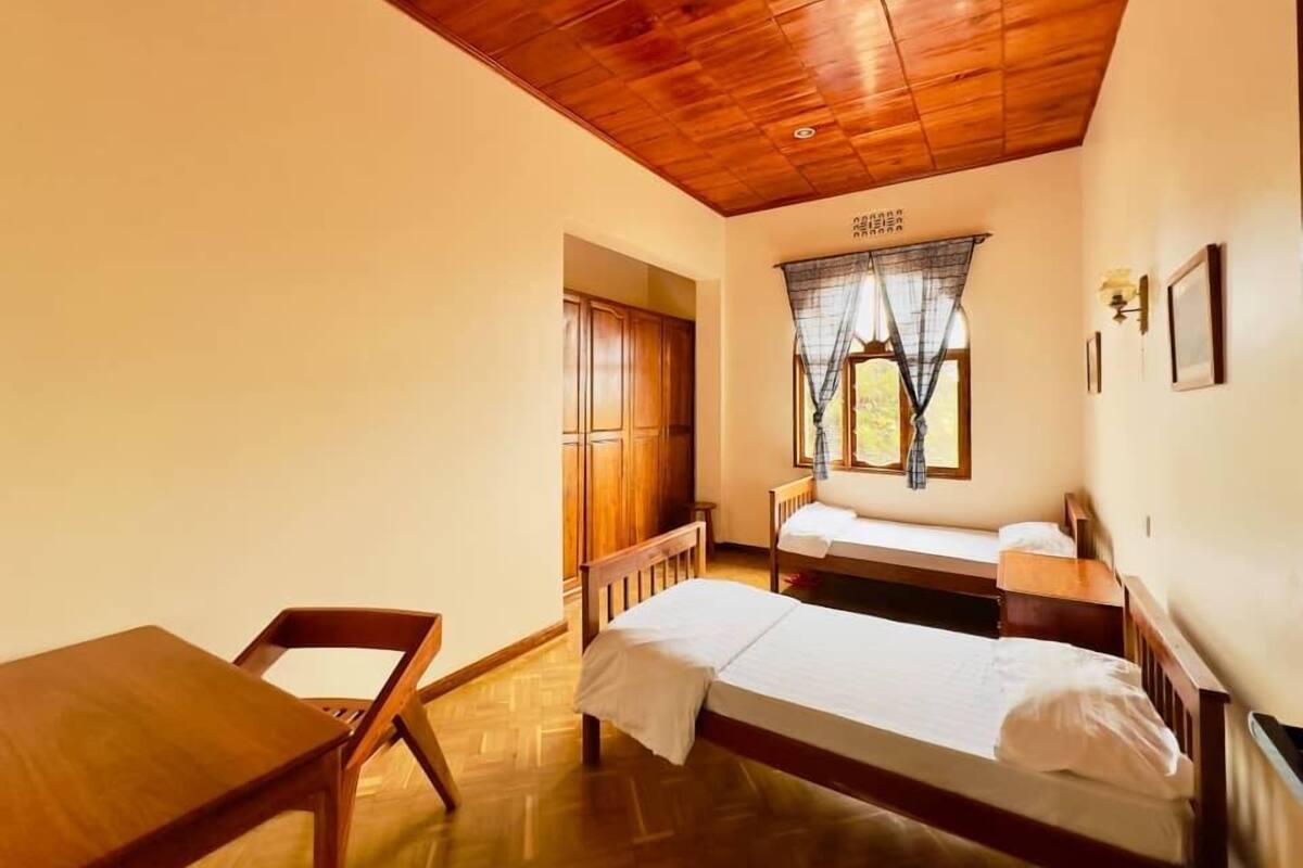 A room with two wooden beds, a wooden table, and a window with curtains.