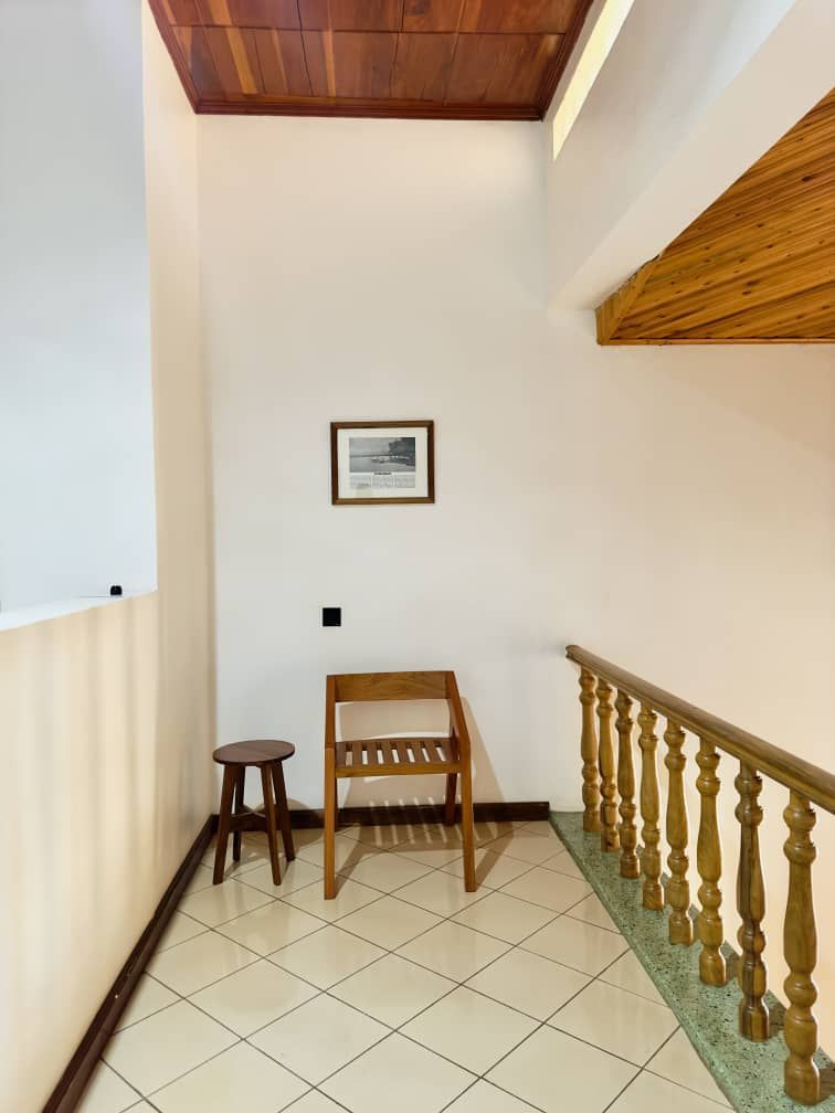 Un coin de pièce avec un banc en bois, un petit tabouret, un tableau encadré accroché au mur et un escalier avec des balustrades en bois.
