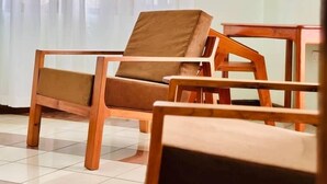 Une pièce avec une chaise en bois et une table, un sol carrelé et une fenêtre ornée de rideaux légers.