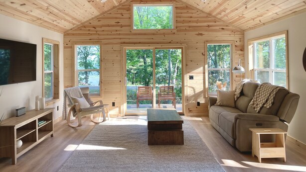 A spacious cabin with a high ceiling, wooden walls, and large windows offering views of the outdoors. - Modern Design - Fire Pit - Lake Access (Montello)