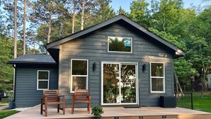 A two-story house with a dark gray exterior, large windows, and a small porch with two wooden chairs. - Modern Design - Fire Pit - Lake Access (Montello)