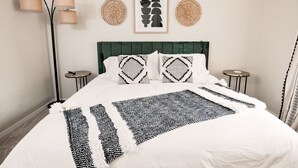 A neatly made bed with a patterned throw, a green upholstered headboard, and two bedside tables with lamps. - Entire Home Close To Everything (Albuquerque)