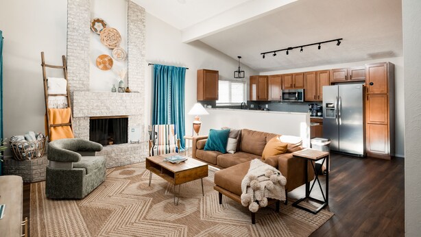 A modern living room with a fireplace, a sofa, a coffee table, and a kitchen area with wooden cabinets and stainless steel appliances. - Entire Home Close To Everything (Albuquerque)
