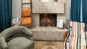 A cozy living room with a brick fireplace, a wooden ladder, a patterned armchair, and a colorful sofa. - Entire Home Close To Everything (Albuquerque)