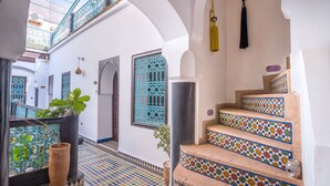 Une cour avec un sol carrelé, un escalier orné de carreaux colorés et une plante en pot.