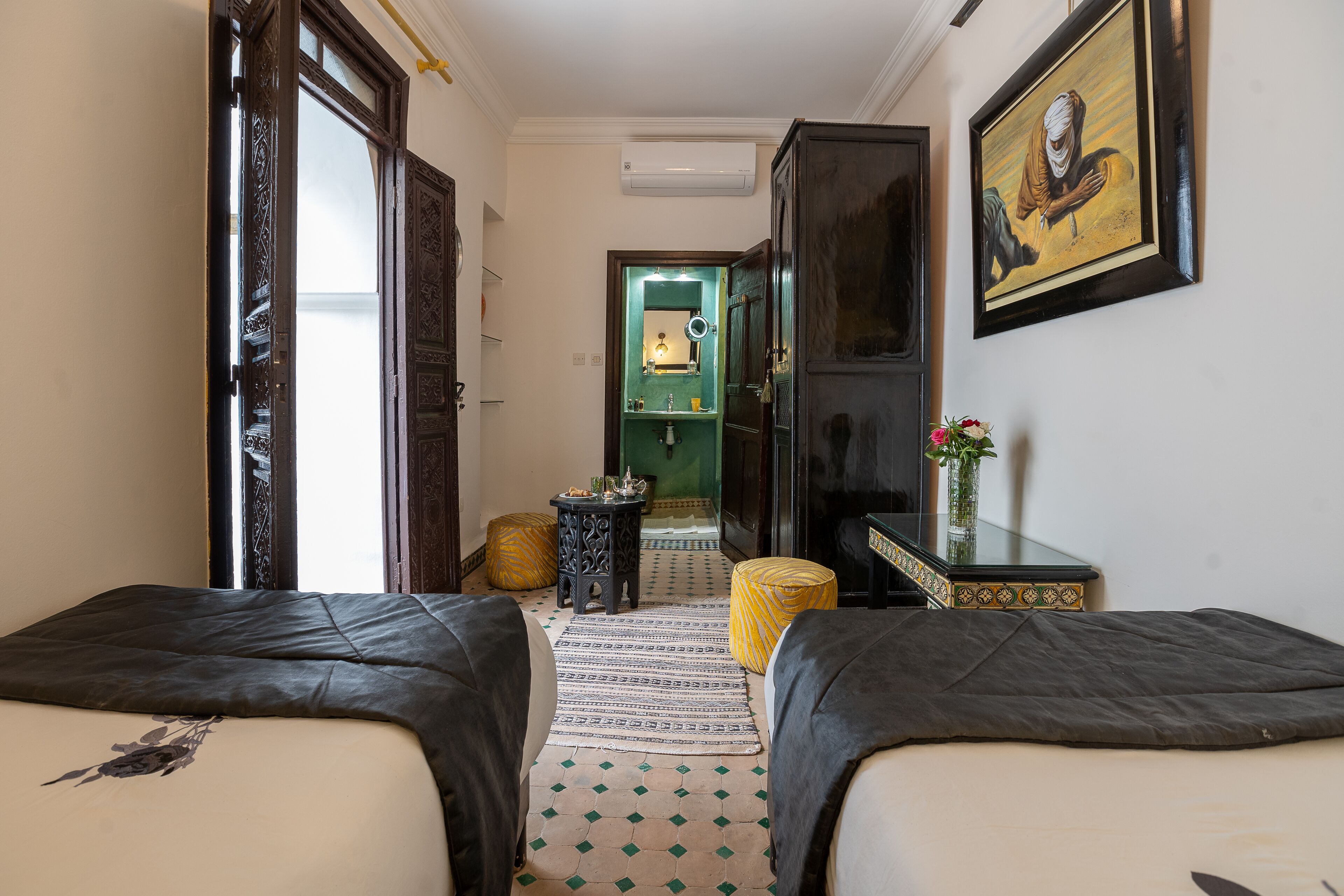 A hotel room with two beds, a mirror, a small table with a vase, and a painting on the wall.