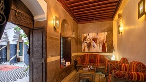 Un intérieur marocain traditionnel, avec un sol à motifs, un plafond en bois et un canapé agrémenté de coussins à motifs.
