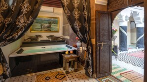 Une salle de bain avec une baignoire, un petit tabouret sur lequel est posée une théière, et un tableau accroché au mur.