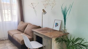 A cozy room with a sofa, a small desk, a chair, a lamp, and decorative items on the wall.