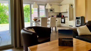A modern kitchen with white cabinets, a microwave, and a refrigerator. There is a dining area with a table and chairs, and a sofa in the living room. - Cozy vacation home with sauna, fireplace, garden and boat (pet-friendly) (Röbel/Müritz)