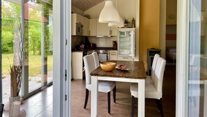 A modern kitchen with a dining area, large windows, and a hanging light fixture.