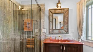 Ein Badezimmer mit einer Duschkabine aus Holz, einem großen Spiegel und einem roten Waschbecken mit Holdeinbauschränken.