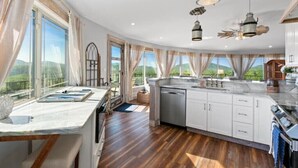 Eine geräumige Küche mit einer großen Kochinsel, weißen Schränken und Blick ins Freie.