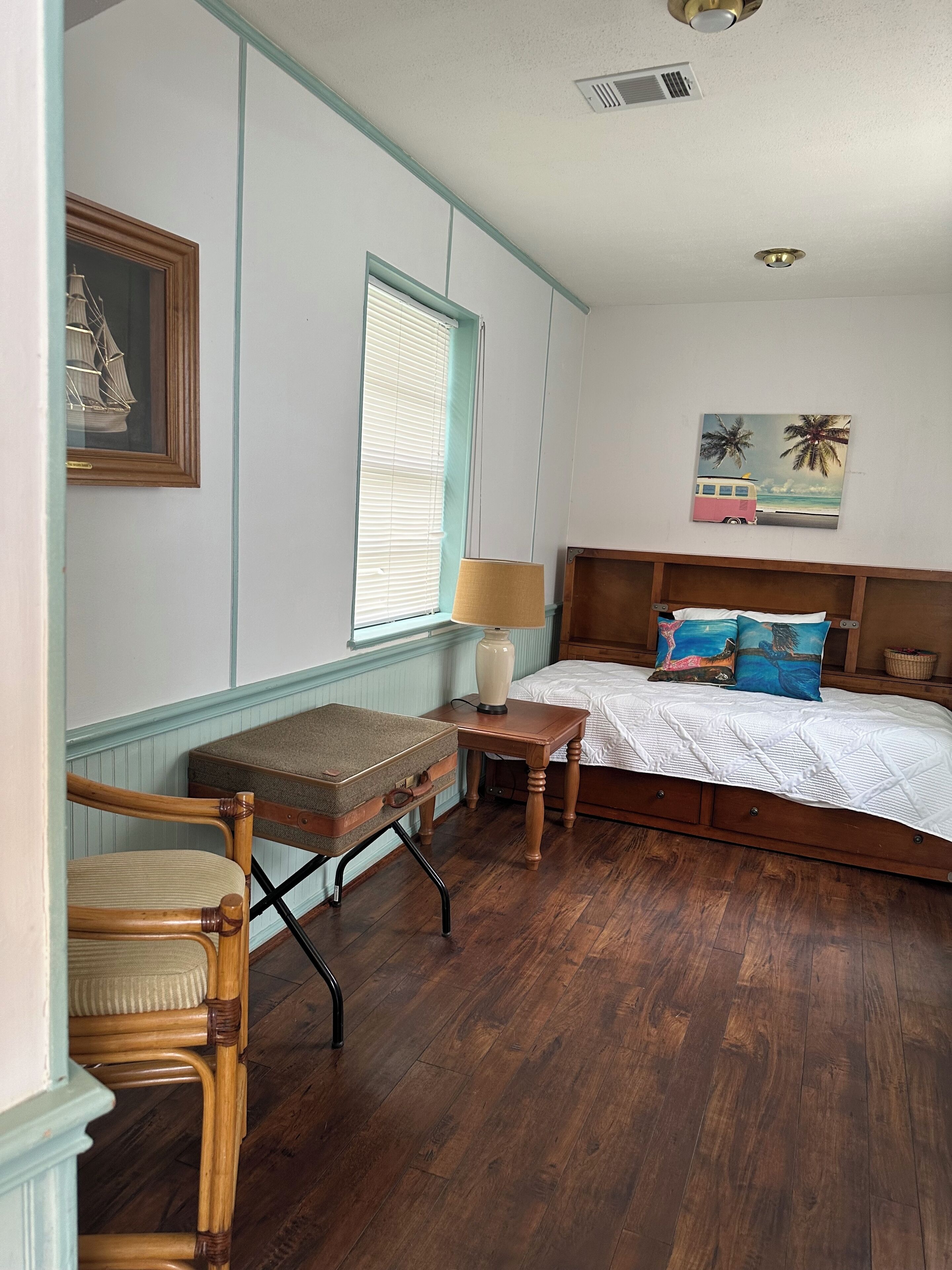 A bedroom with a wooden bed, a nightstand, a lamp, a chair, and a window with blinds.