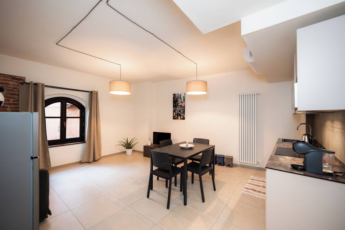 Una cocina moderna con comedor, que incluye una mesa con sillas, luces colgantes, una planta en maceta y un radiador.